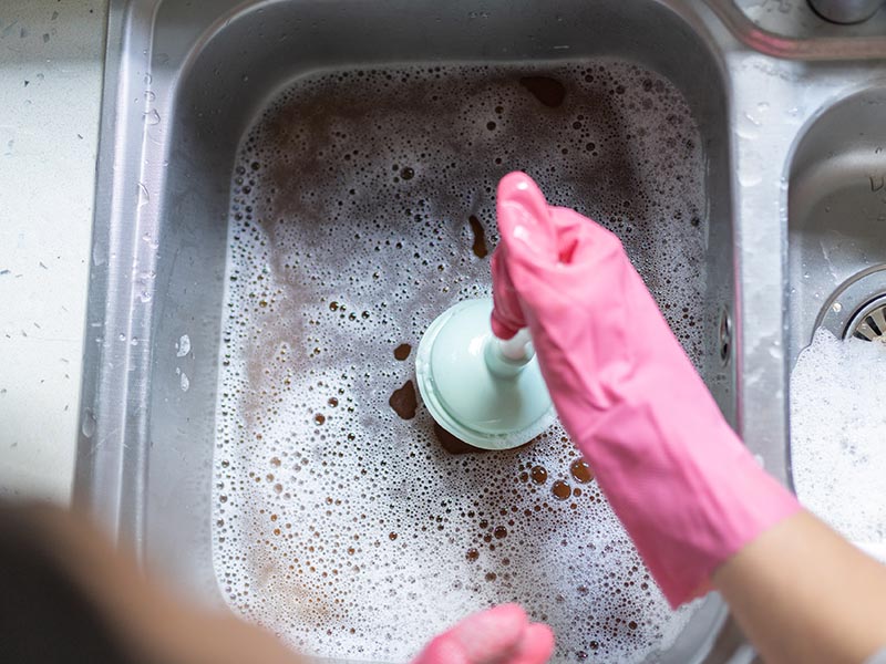 Homeowner attempting to clear a kitchen sink clog with a small plunger