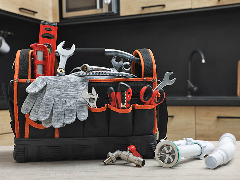 A work bag with plumbing tools sitting on a kitchen counter with a sink in the background.
